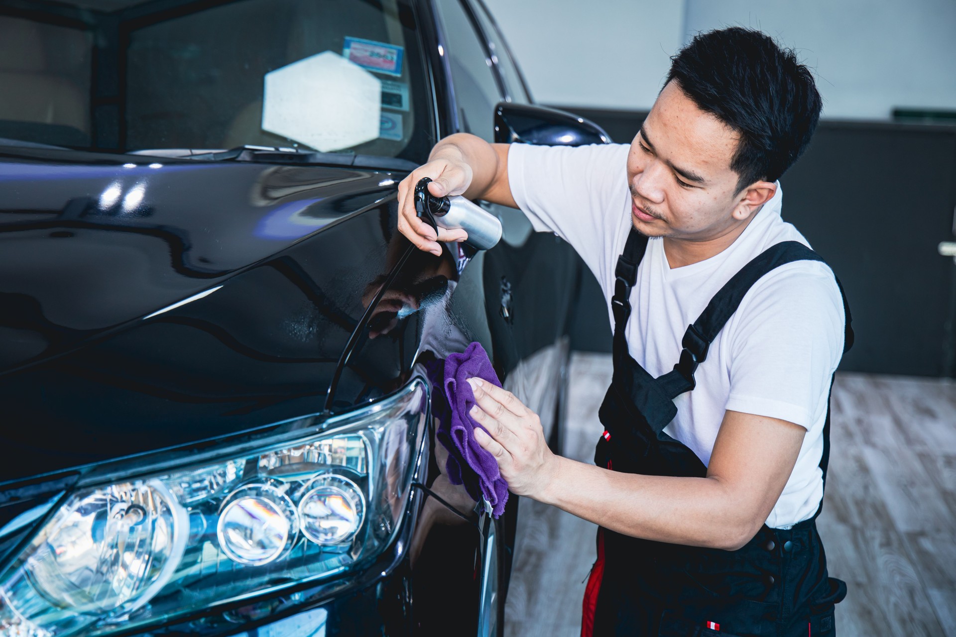 Worker wearing an apron is spraying car varnish and use a cloth to polish the cars in the garage.